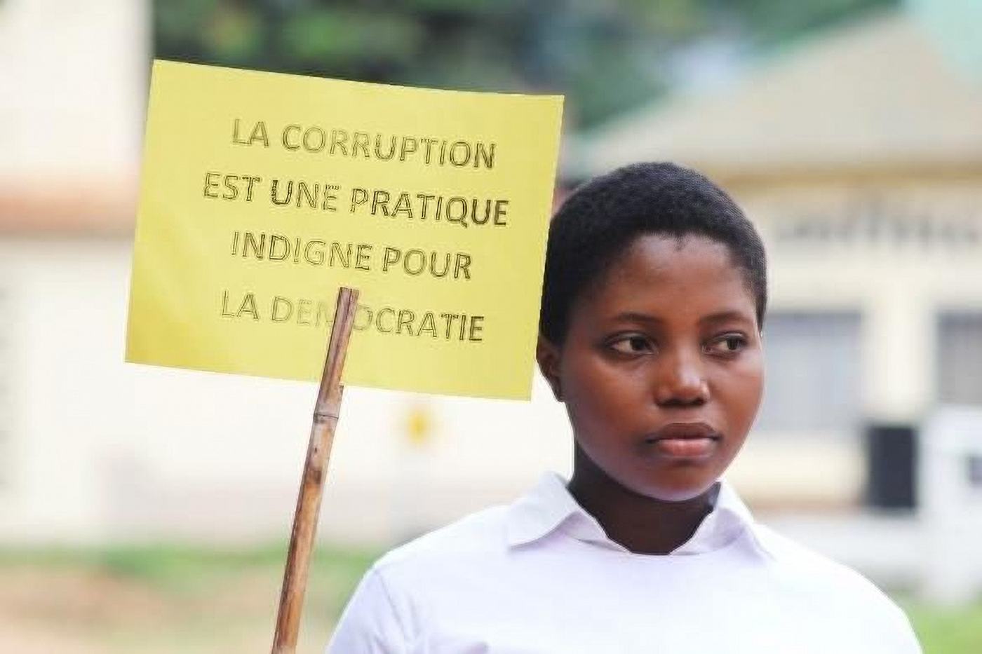 A student holds a placard reading “La corruption est une pratique indigne pour la démocratie”